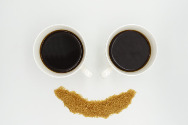 两个瓷咖啡杯，里面盛着美式咖啡，撒上白底笑脸形状的糖图片下载