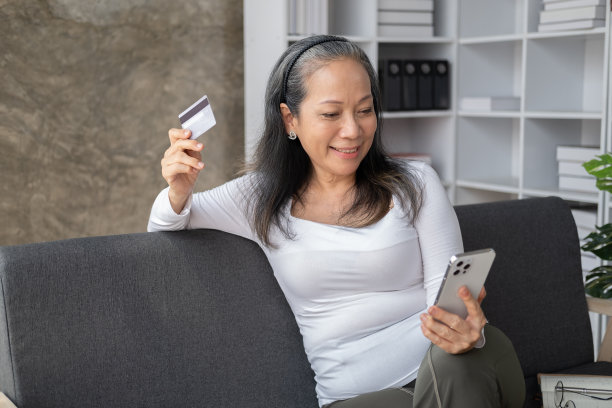 被释放的亚洲老年妇女坐在沙发上用智能手机在网上购物。图片下载
