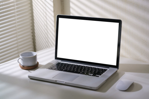 在明亮的办公室内部，白色的桌子上放着空显示屏的笔记本电脑和一杯咖啡。图片下载