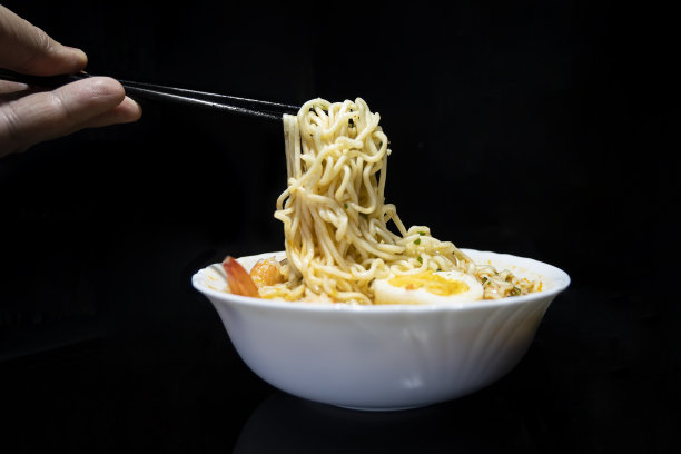 男手在黑色背景的碗里用筷子搅拌方便面。图片下载