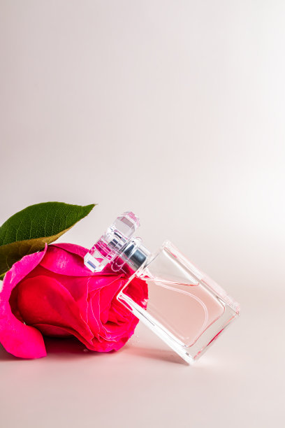 一朵粉色玫瑰的花头上放着一瓶别致的女性香水或淡香水。正面垂直视图。柔和的背景。一个拷贝空间。图片下载