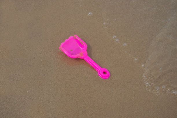 粉色玩具塑料铲在沙滩和海浪上。夏季的概念照片图片下载