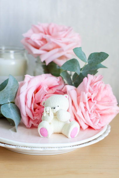 可爱的可食用的泰迪熊玩具由白巧克力和新鲜的牡丹和蜡烛的背景。给宝宝的礼物图片下载
