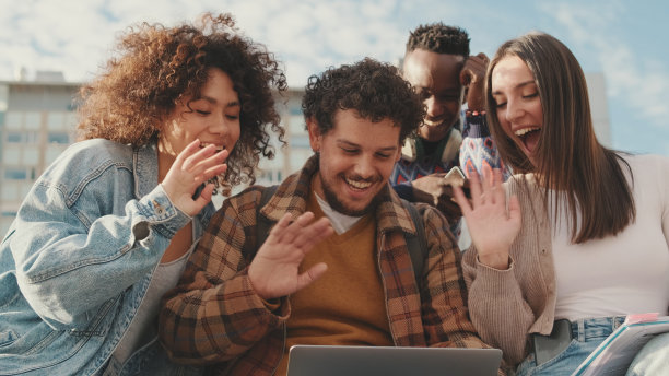 开心微笑的朋友在外面对着笔记本电脑大笑。四个学生聚在一起图片下载