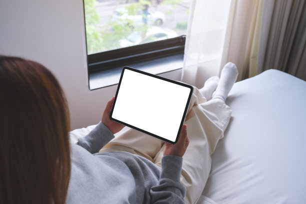 一个女人坐在床上，拿着空白桌面的数字平板电脑的模拟图像图片下载