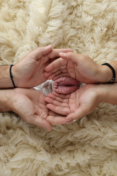 新生儿的脚放在父母的手掌上。父亲和母亲的手掌托着新生婴儿的脚，上面盖着一条白色的弗洛卡蒂毯子。孩子的脚趾、脚后跟和脚的照片。图片下载