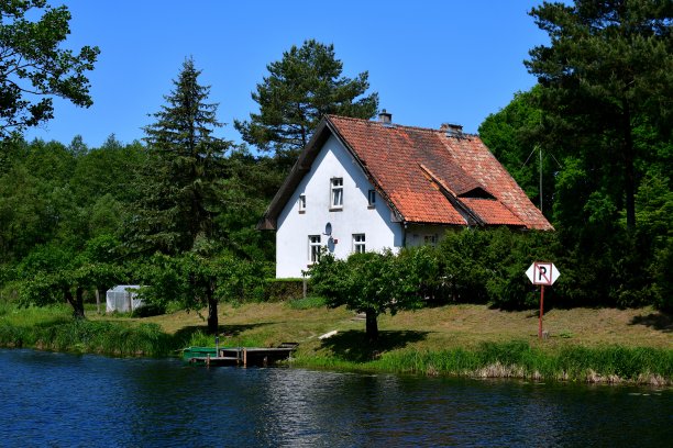 在波兰一个阳光明媚的夏日里，位于一条浅而宽阔的河流岸边，靠近一些果园、森林或沼泽的棚屋、住所或房屋的特写图片下载