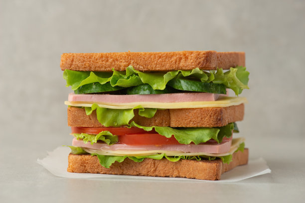 灰色的桌子上放着夹有摩泰台拉、奶酪和西红柿的三明治图片下载