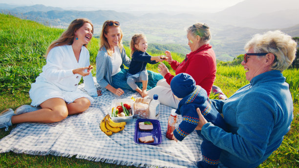 一个大家庭在日出时在山上的绿色小山上野餐图片下载