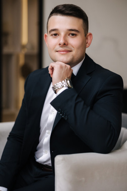 一个穿着优雅深蓝色西装的年轻人坐在家里的椅子上。图片下载