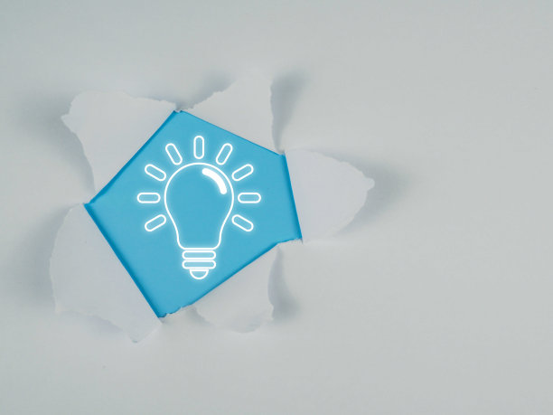 明亮的灯泡在蓝色的背景与撕破的白纸。图片下载
