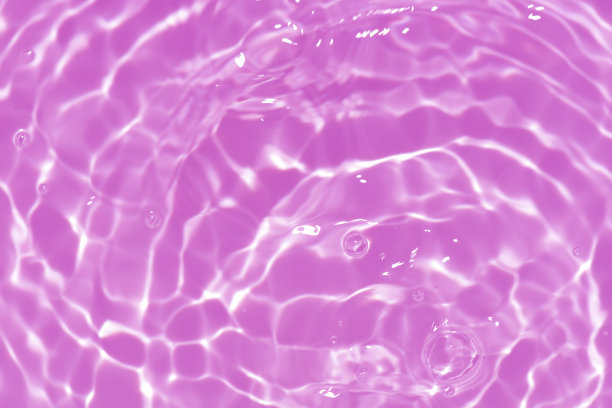 紫色的水面上泛起涟漪。散焦模糊透明粉红色透明平静水面纹理与飞溅和泡沫。水波与闪亮的图案纹理背景。图片下载