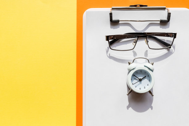 最小的组成与透明的笔记本，眼镜，笔和小时钟在黄色的桌子上，平躺，模拟，俯视图。办公用品和眼镜。模型表示。时间管理。本空间图片下载