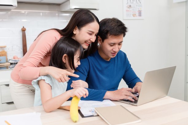 美丽的亚洲女人可爱的女孩看着笔记本电脑的屏幕帅气的男人在家里的桌子上工作这是一个新的正常的家庭生活。图片下载