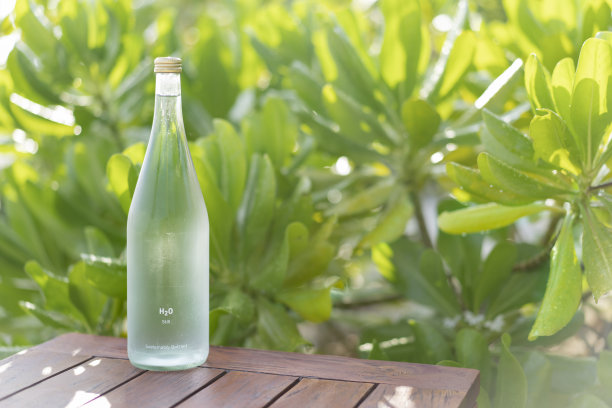 玻璃瓶里的水，背景是郁郁葱葱的绿叶图片下载