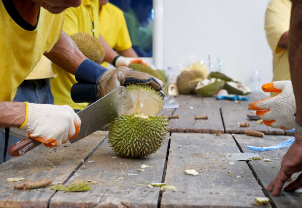 在泰国街头食品市场，一名亚洲男子正在为买家手工剥榴莲。近距离的商人的手正在用刀剥榴莲，榴莲是泰国的水果之王。图片下载