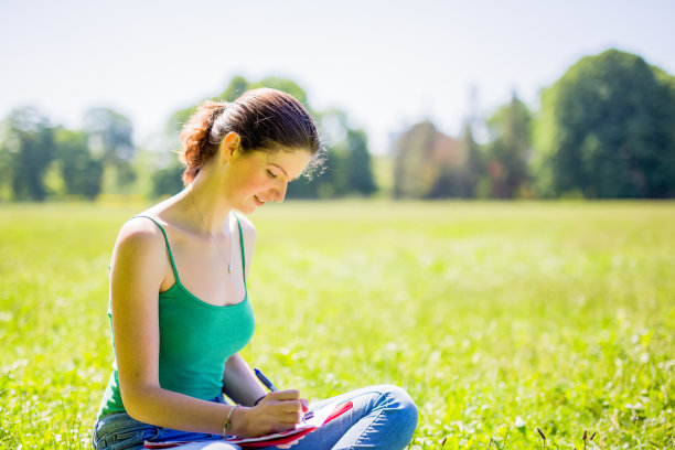 年轻女子坐在公园里写作图片下载