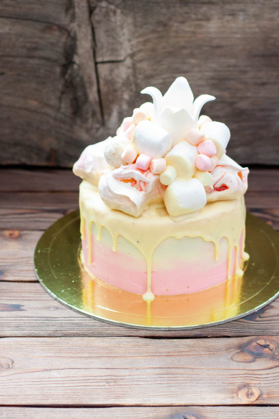 鲜嫩的粉色生日蛋糕，在质朴的背景上点缀着融化的白巧克力、糖冠、蛋白霜和棉花糖图片下载
