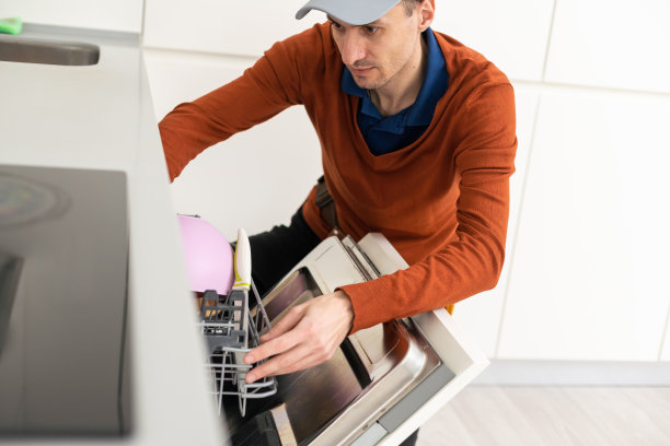 一个穿着特殊衣服的人或服务人员用螺丝刀将洗碗机固定在工作台上或移走。图片下载