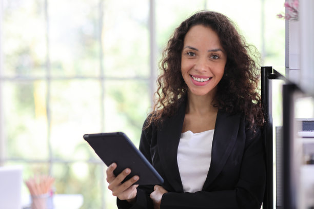 自信而美丽的年轻非洲女商人的肖像，带着快乐的微笑，站在现代办公室里，看着相机，使用平板电脑。成功经营理念图片下载