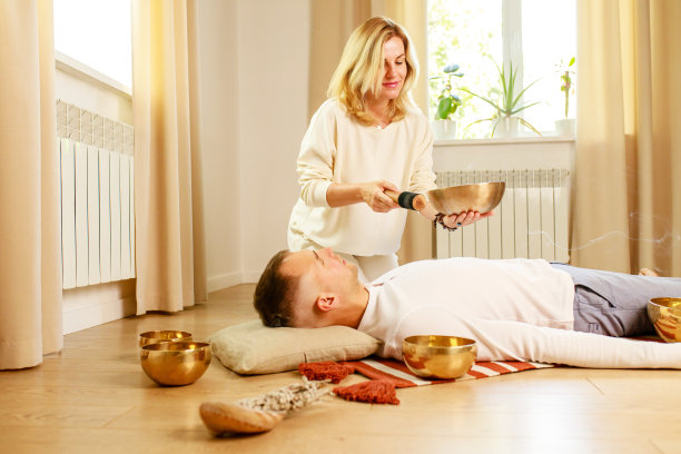 女子在玩藏式唱碗，为男子按摩冥想图片下载