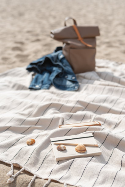 旅行者的背包、一本日记本和一套铅笔躺在沙滩上的毯子上。图片下载