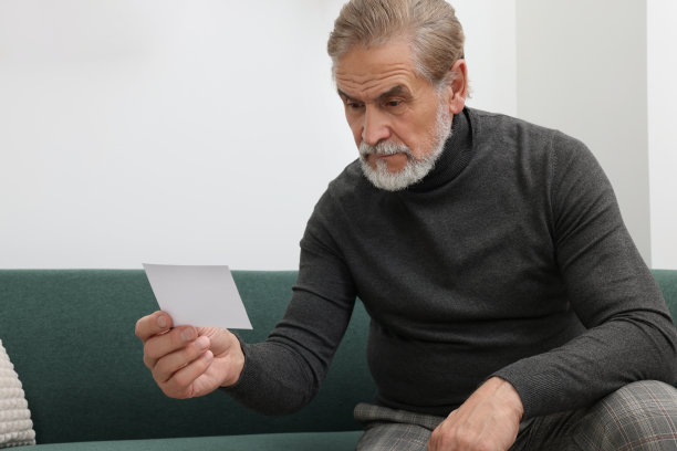 心烦意乱的老人拿着照片坐在家里的沙发上。孤独的概念图片下载