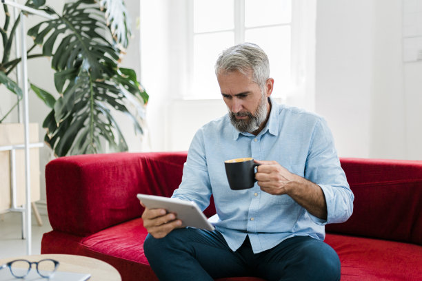 严肃的老年人使用数码平板电脑，喝咖啡，在家工作图片下载