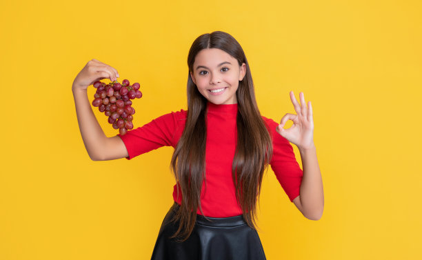 十几岁的孩子微笑着拿着黄色背景上的一串葡萄图片下载