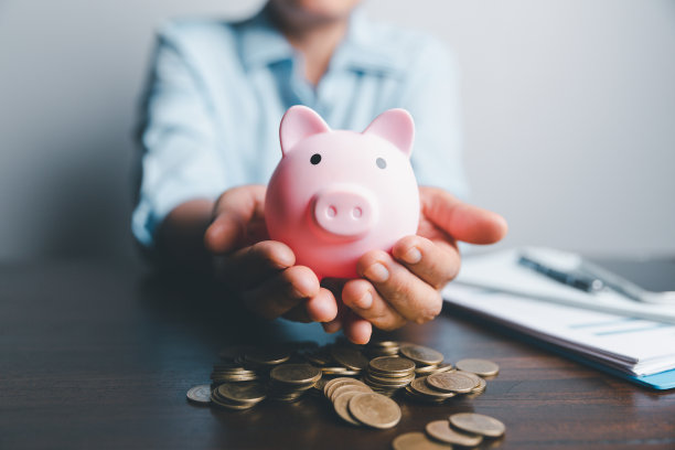 商业亚洲女性将硬币放在木桌背景上的扑满里，存钱理财理念，理财，投资，理财规划。财务规划退休存款图片下载