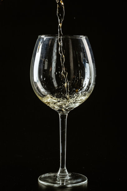 白葡萄酒倒在酒杯里，背景是黑色的图片下载