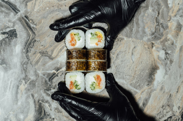 寿司卷，包在紫菜里，厨师戴着手套用刀切。寿司是用生鱼做的图片下载