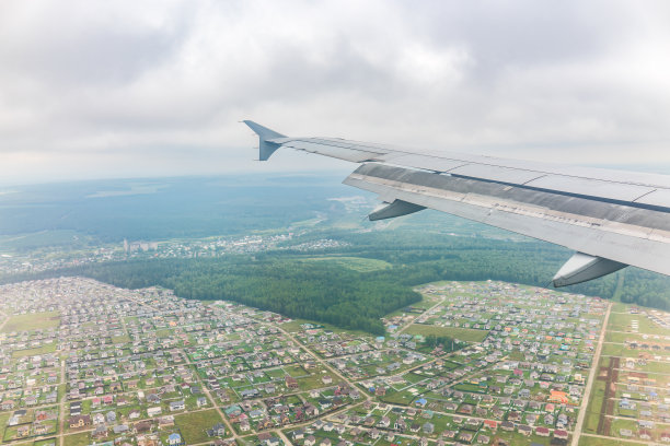 飞机机翼的视图，蓝天和绿色的土地在着陆。飞机窗口视图。图片下载