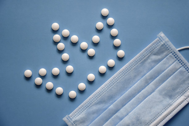 医用防护口罩和蓝色背景白色圆丸，俯视图，平放。冠状病毒，由药丸制成的冠状图像。图片下载
