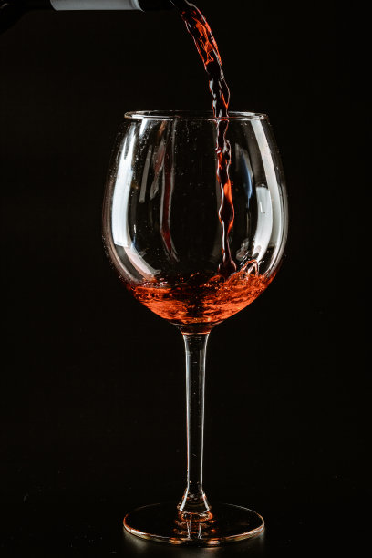 红酒被倒进酒杯里，背景是黑色的图片下载