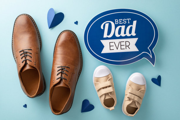 小男孩在父亲节向爸爸表达爱意。父亲的皮鞋，儿子的运动鞋，心和问候匾在淡蓝色的背景俯视图图片下载