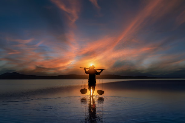 夕阳西下，农夫背着盐走回家的剪影。旅游景观和目的地图片下载