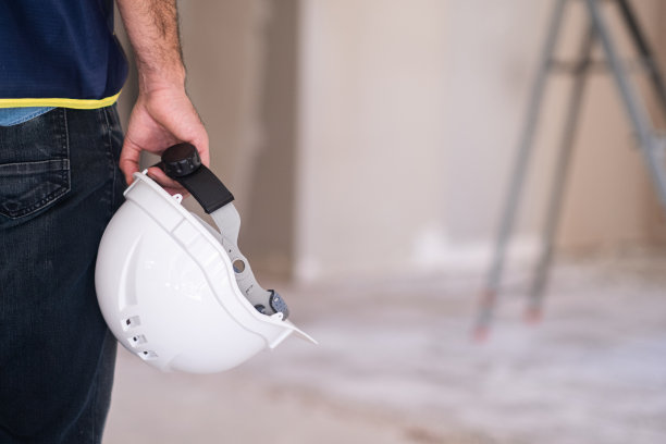 在未完工的房间里，专业工程师手拿白色防护安全帽抵着梯子图片下载