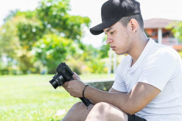一个年轻的拉丁裔视频博主的特写，他手里拿着相机，看着他为自己的社交媒体频道录制的视频图片下载