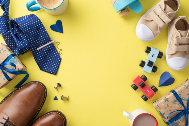 与爸爸和小儿子度过一个特别的父亲节。顶视图的皮鞋，婴儿运动鞋，领带，袖扣，汽车玩具，可可，和礼盒上的黄色背景与空间的文字图片下载