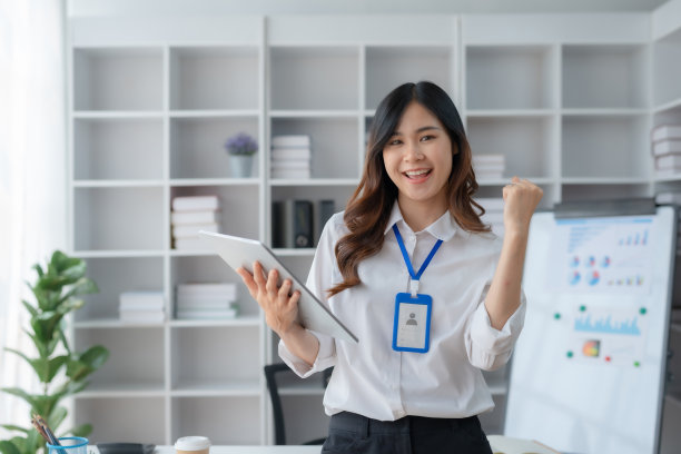 快乐的亚洲女商人举起胜利的手，开心地拿着数码平板电脑微笑。工作中成功的概念。图片下载