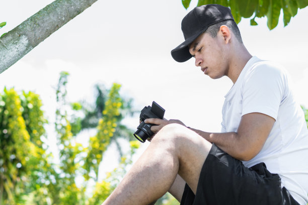 拉丁影响者坐在树下的草地上看他用相机拍的照片图片下载