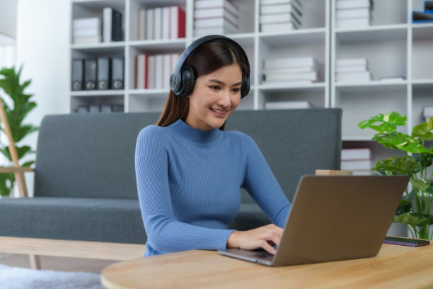 一个快乐的年轻亚洲女性的肖像，在家里用耳机和笔记本电脑听音乐。图片下载