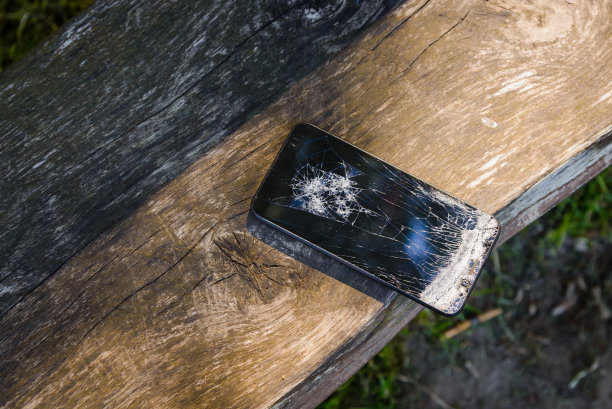 在公园的木凳上摔坏了手机。屏幕破碎的智能手机。夏日公园日。图片下载