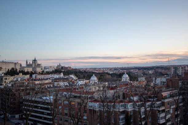 这是一张令人印象深刻的马德里全景照片。这张照片捕捉到了这座城市的天际线，标志性的摩天大楼和历史建筑沐浴在夕阳的柔和光线中。天空呈现出温暖的色调和分散的云，增加了d图片下载