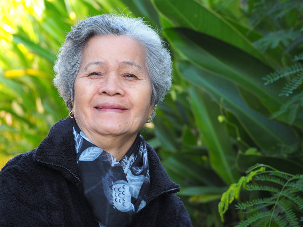 一位年长的亚洲妇女站在户外，微笑着看着镜头。图片下载