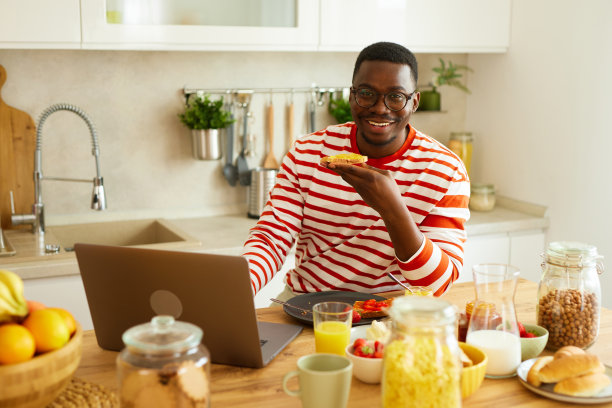 一个非裔美国人一边在家享用早餐一边使用笔记本电脑图片下载