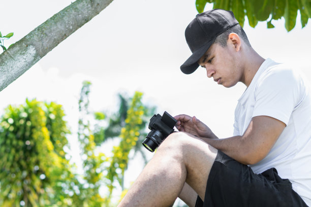 年轻的拉丁裔男子，坐在现场观看他在社交媒体摄像机上录制的内容。图片下载