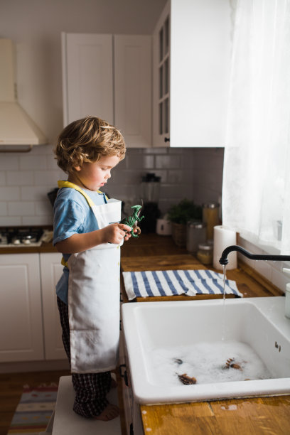 小男孩在厨房水槽里玩耍，用水洗恐龙玩具的侧视图图片下载