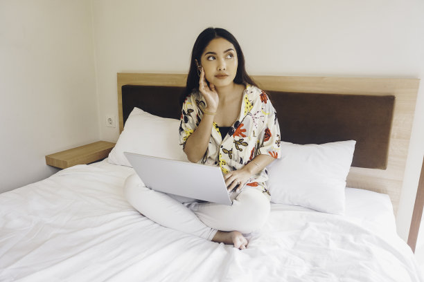 年轻女子在床上工作，一边看一边沉思图片下载